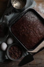 Homemade chocolate sponge cake and ingredients on wooden table, flat lay