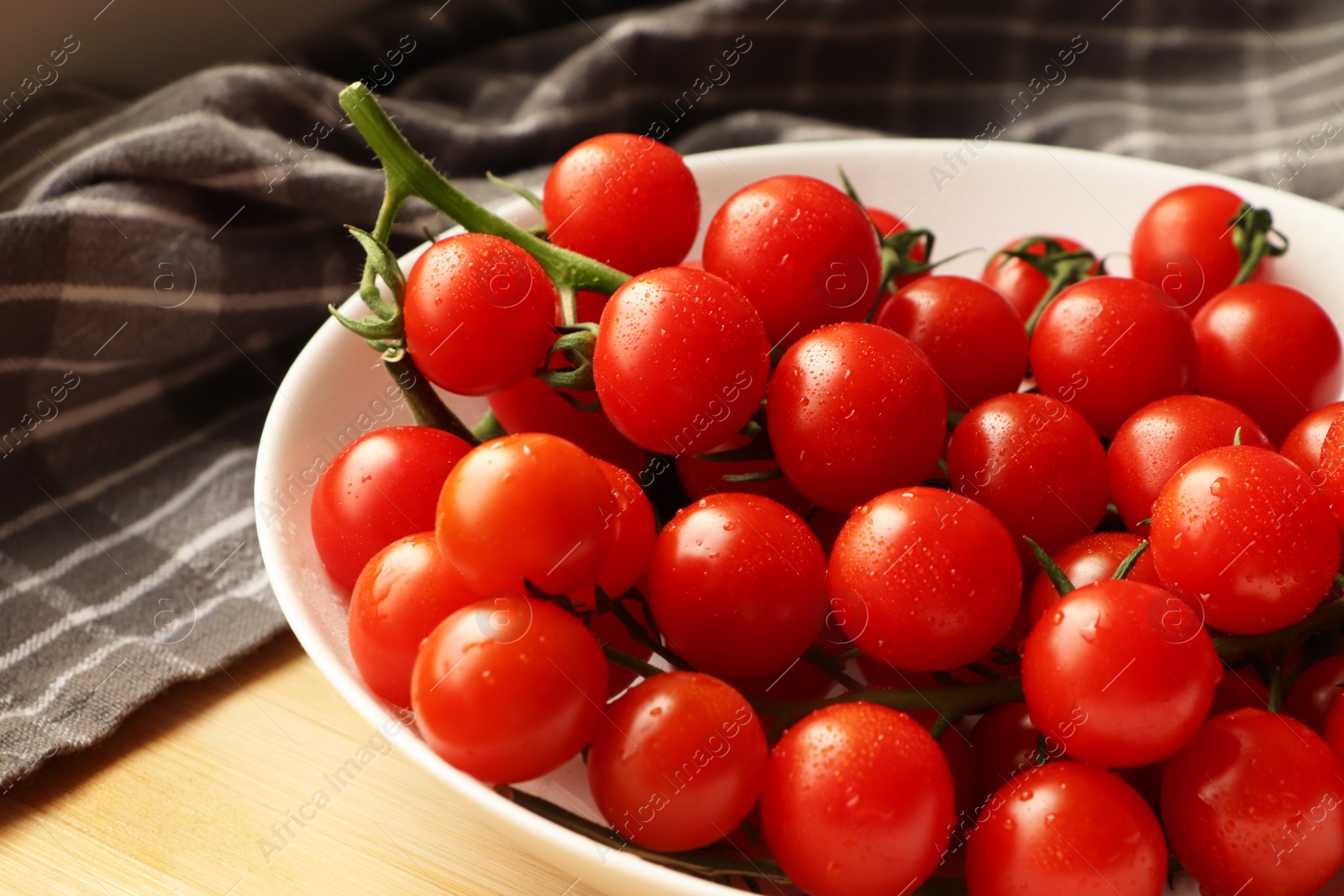 Photo of Plate of ripe whole cherry tomatoes with water drops on wooden table, closeup