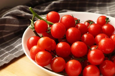 Photo of Plate of ripe whole cherry tomatoes with water drops on wooden table, closeup