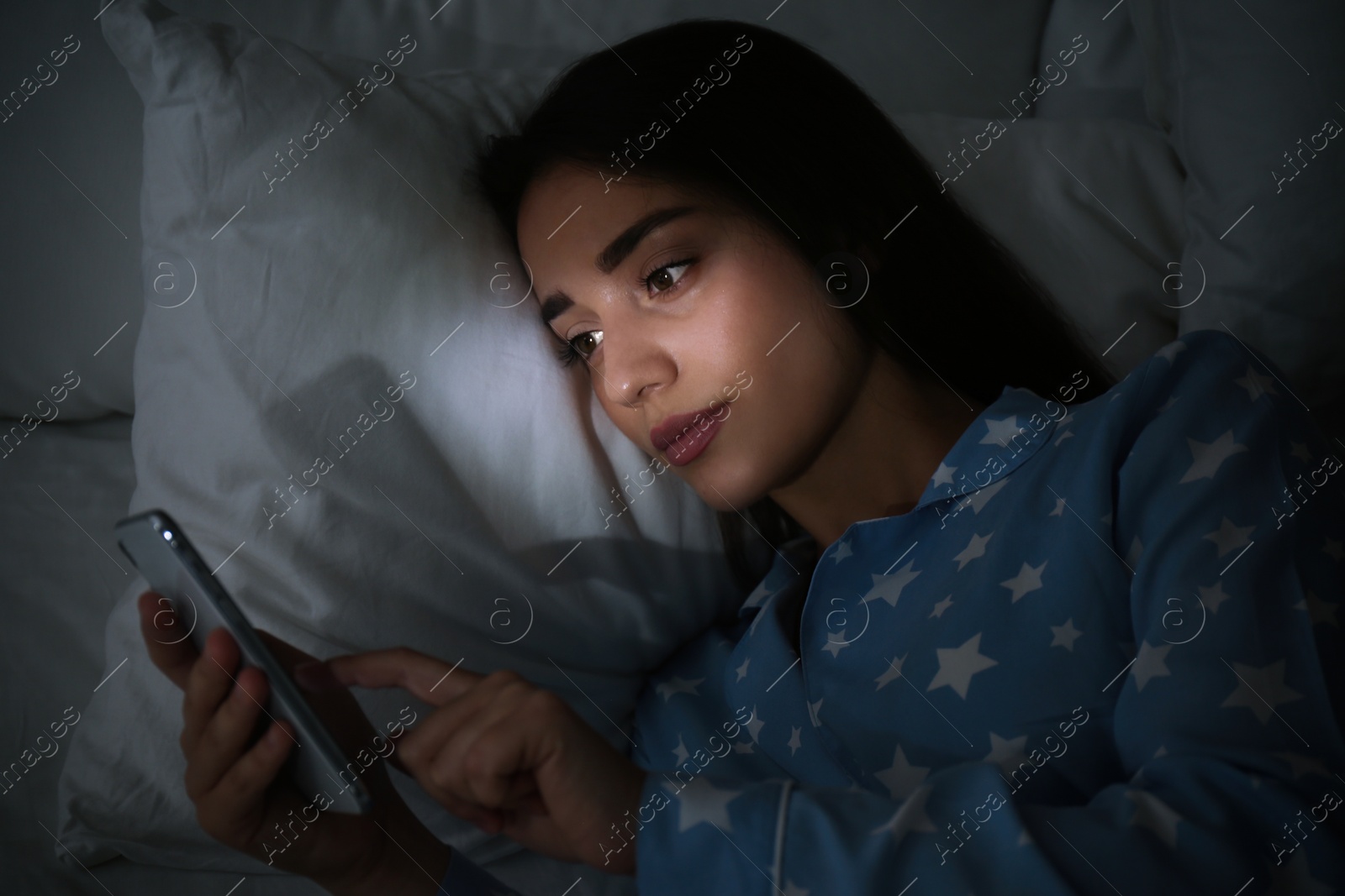 Photo of Young woman using mobile phone in dark bedroom