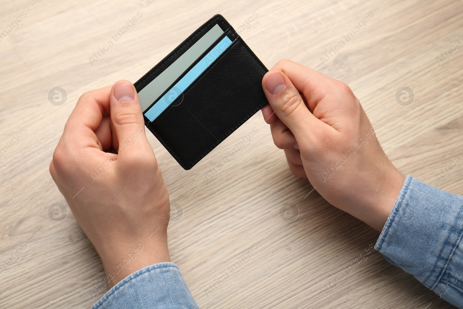 Photo of Man holding leather business card holder with cards at wooden table, closeup