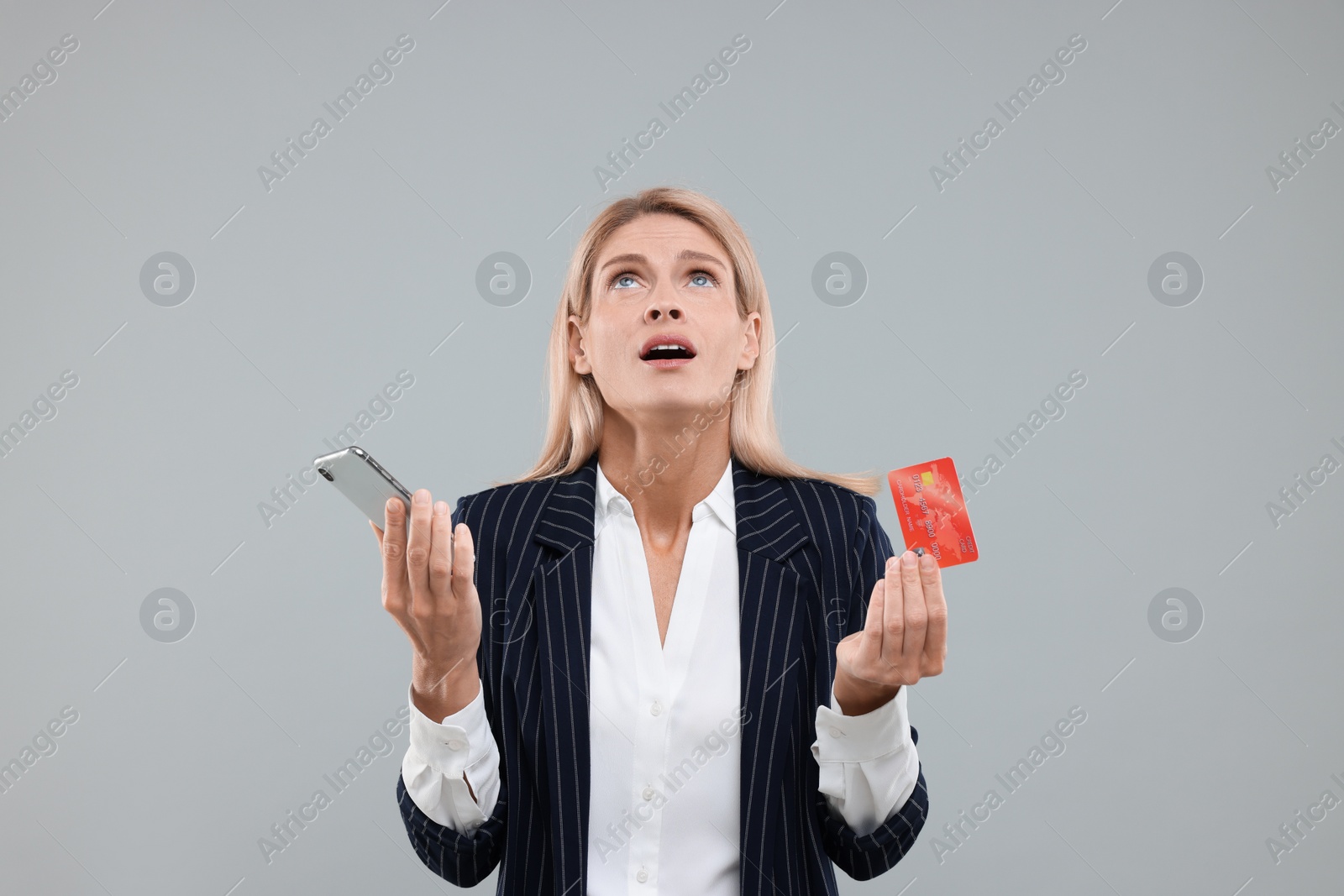 Photo of Emotional woman with credit card and smartphone on grey background. Be careful - fraud