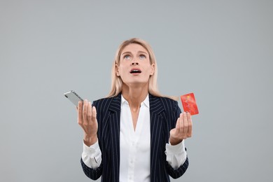 Photo of Emotional woman with credit card and smartphone on grey background. Be careful - fraud