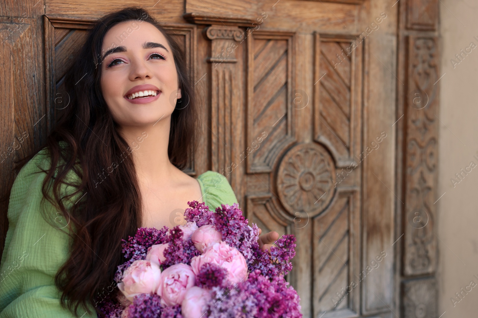 Photo of Beautiful woman with bouquet of spring flowers near wooden door, space for text