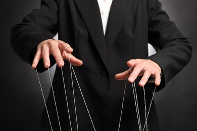 Photo of Woman in suit pulling strings of puppet on dark background, closeup