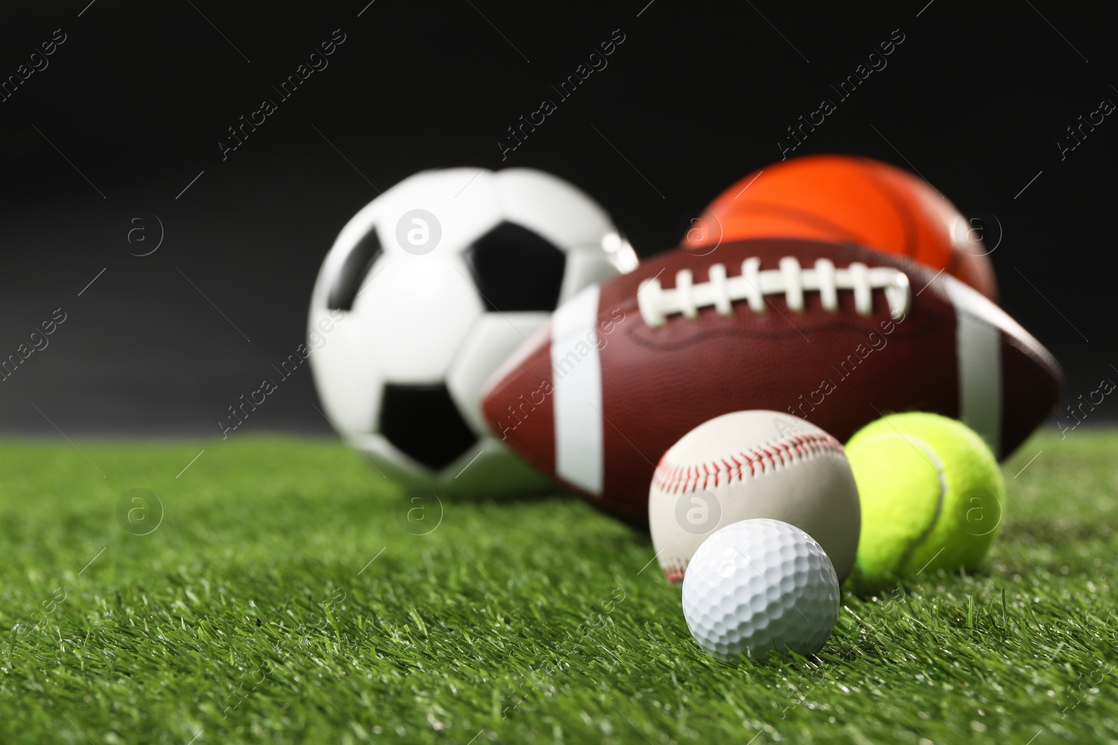 Photo of Many different sports balls on green grass against black background, closeup. Space for text