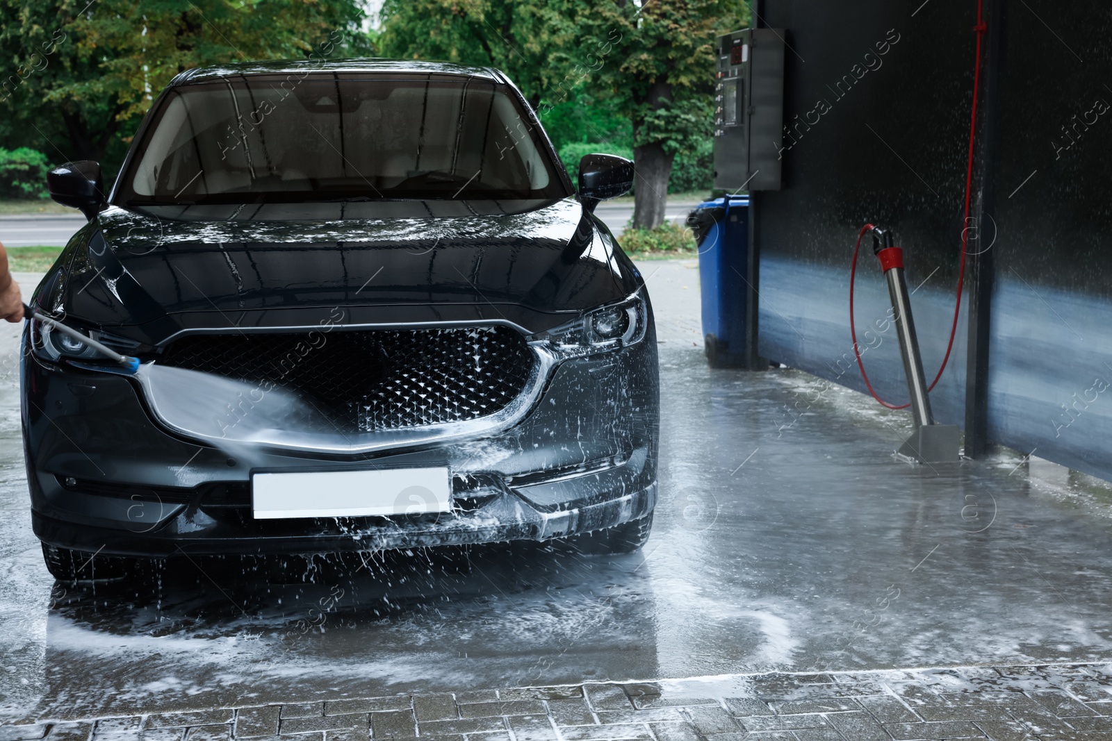 Photo of Man washing auto with high pressure water jet at car wash, closeup