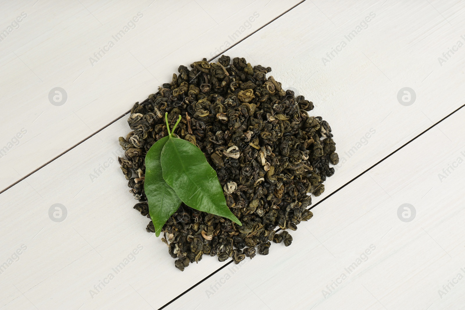 Photo of Heap of dried green tea leaves on white wooden table, top view