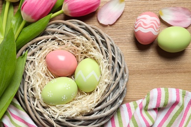 Flat lay composition with painted Easter eggs and tulips on wooden table