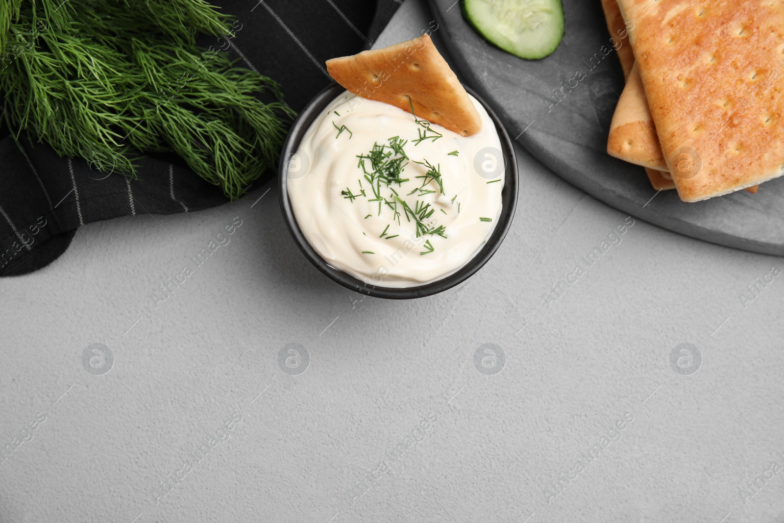 Photo of Tasty creamy dill sauce, crackers and ingredients on grey table, flat lay. Space for text