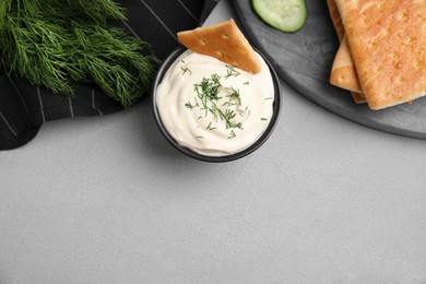 Photo of Tasty creamy dill sauce, crackers and ingredients on grey table, flat lay. Space for text