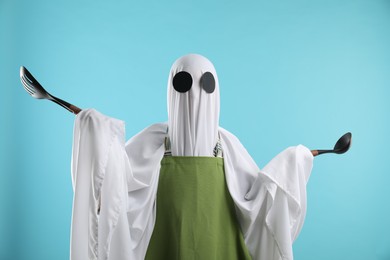 Photo of Woman in ghost costume and apron with kitchen set on light blue background