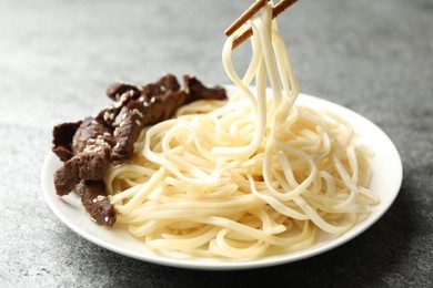 Photo of Chopsticks with tasty cooked rice noodles over plate on grey table