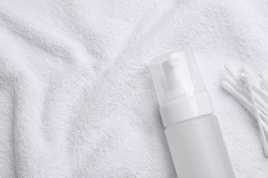 Bottle of face cleansing product and cotton buds on white towel, flat lay. Space for text