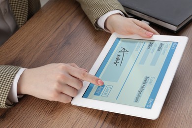 Image of Electronic signature. Woman using tablet at wooden table, closeup