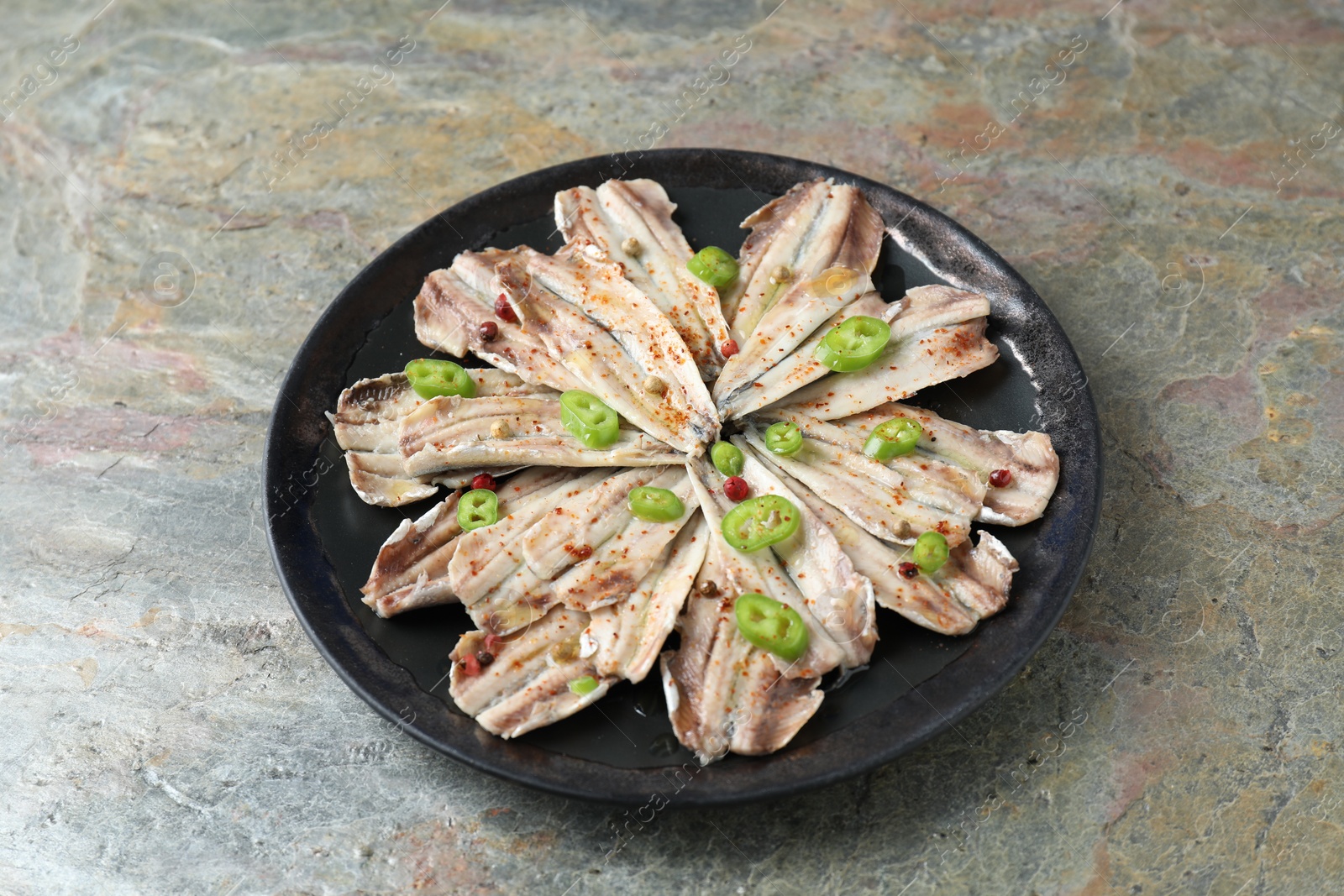 Photo of Tasty pickled anchovies with spices on textured table