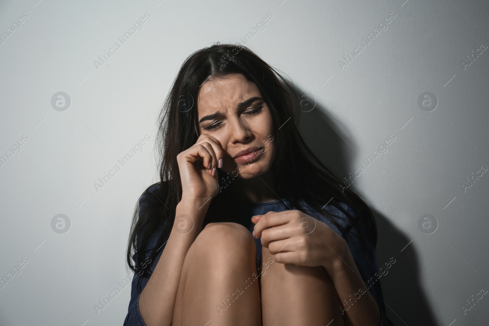 Photo of Abused young woman crying near white wall. Domestic violence concept