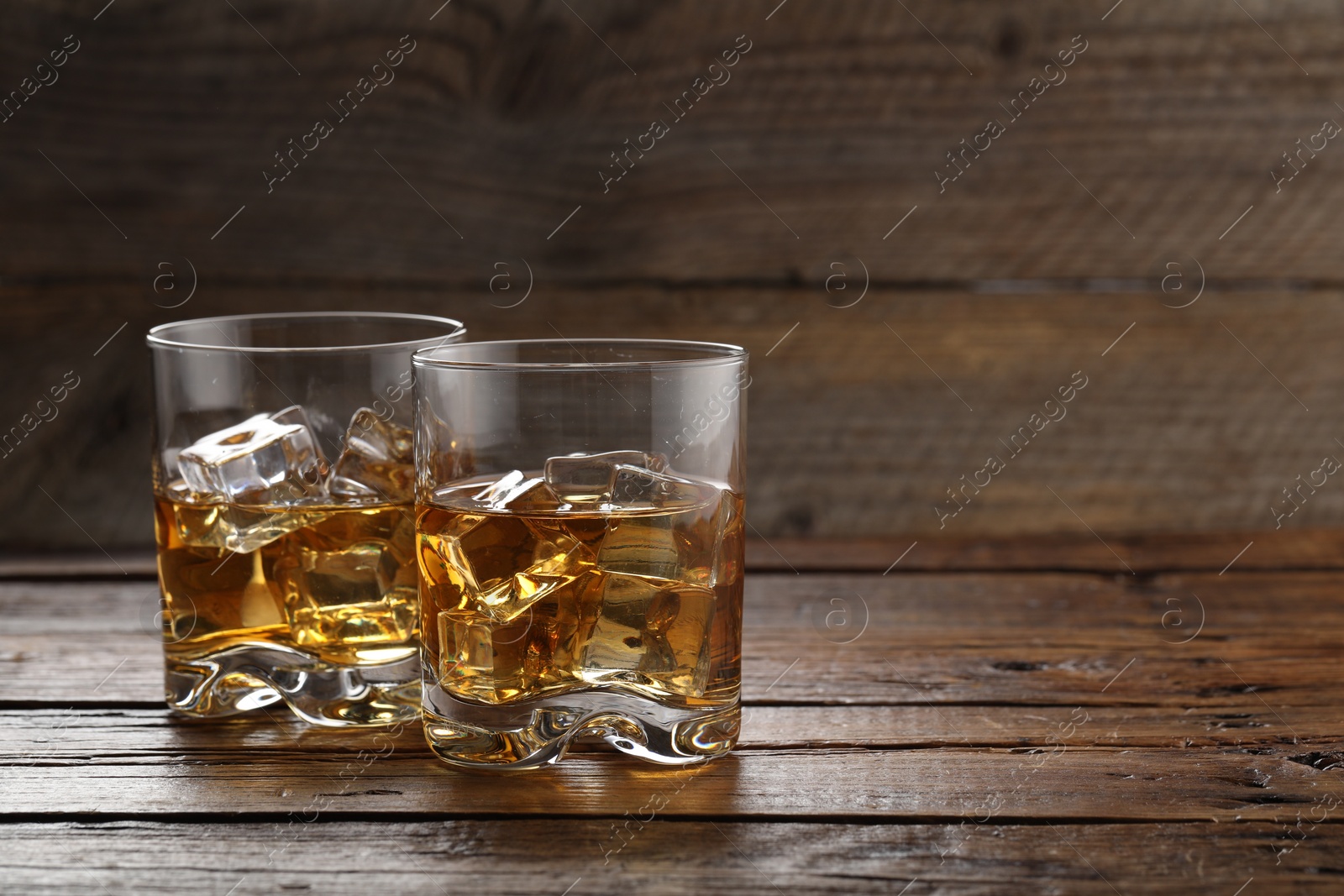 Photo of Whiskey with ice cubes in glasses on wooden table, closeup. Space for text