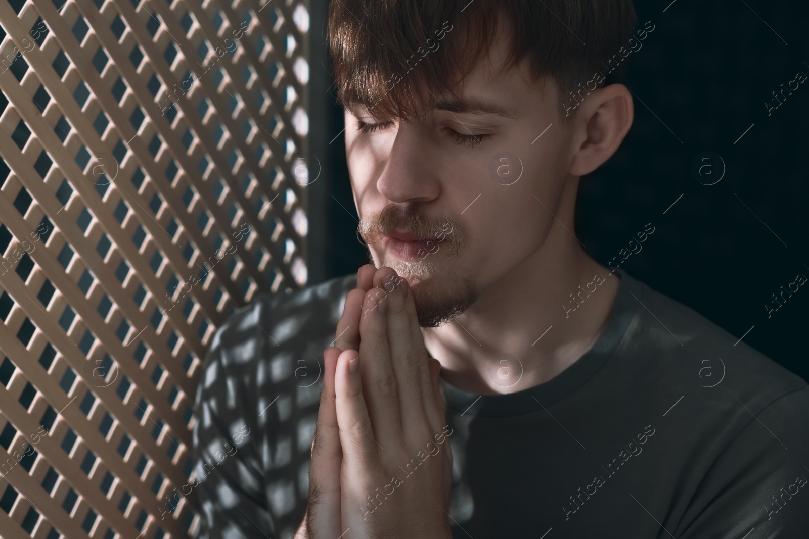 Photo of Man praying during confession near wooden window in booth