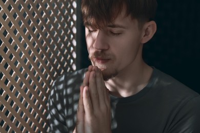 Man praying during confession near wooden window in booth