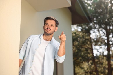 Photo of Angry man pointing near house. Annoying neighbour