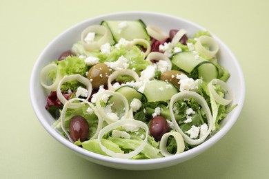 Bowl of tasty salad with leek, olives and cheese on pale green table, closeup