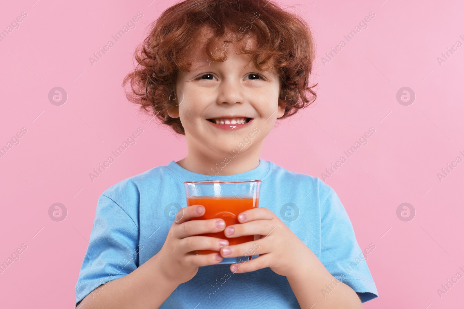 Photo of Cute little boy with glass of fresh juice on pink background