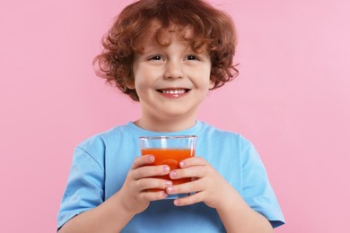 Photo of Cute little boy with glass of fresh juice on pink background