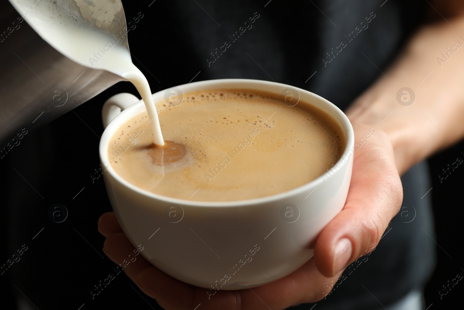 Photo of Woman pouring milk into cup of hot coffee, closeup