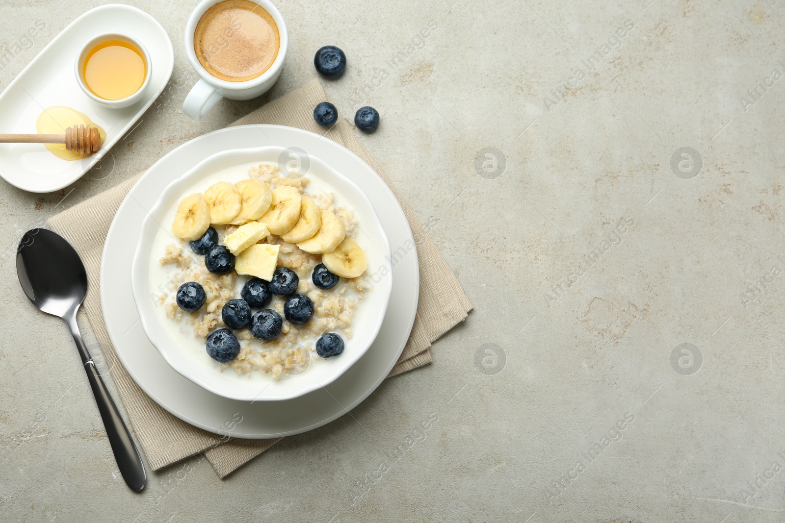 Photo of Tasty oatmeal with banana, blueberries, butter and milk served in bowl on light grey table, flat lay. Space for text