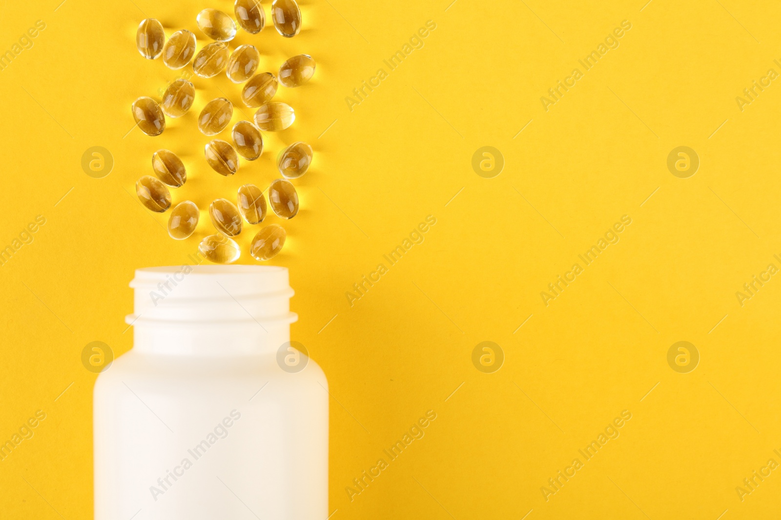 Photo of White medical bottle and vitamin capsules on yellow background, top view. Space for text