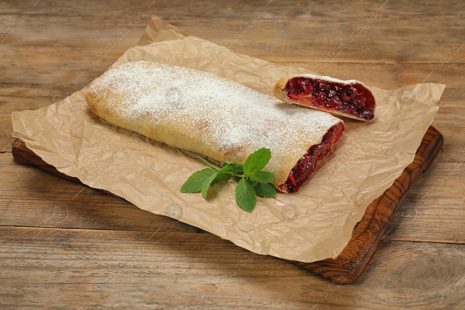 Photo of Delicious strudel with cherries, powdered sugar and mint on wooden table