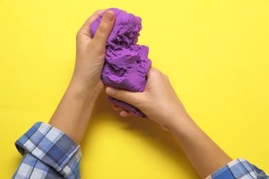 Photo of Woman playing with kinetic sand on yellow background, top view