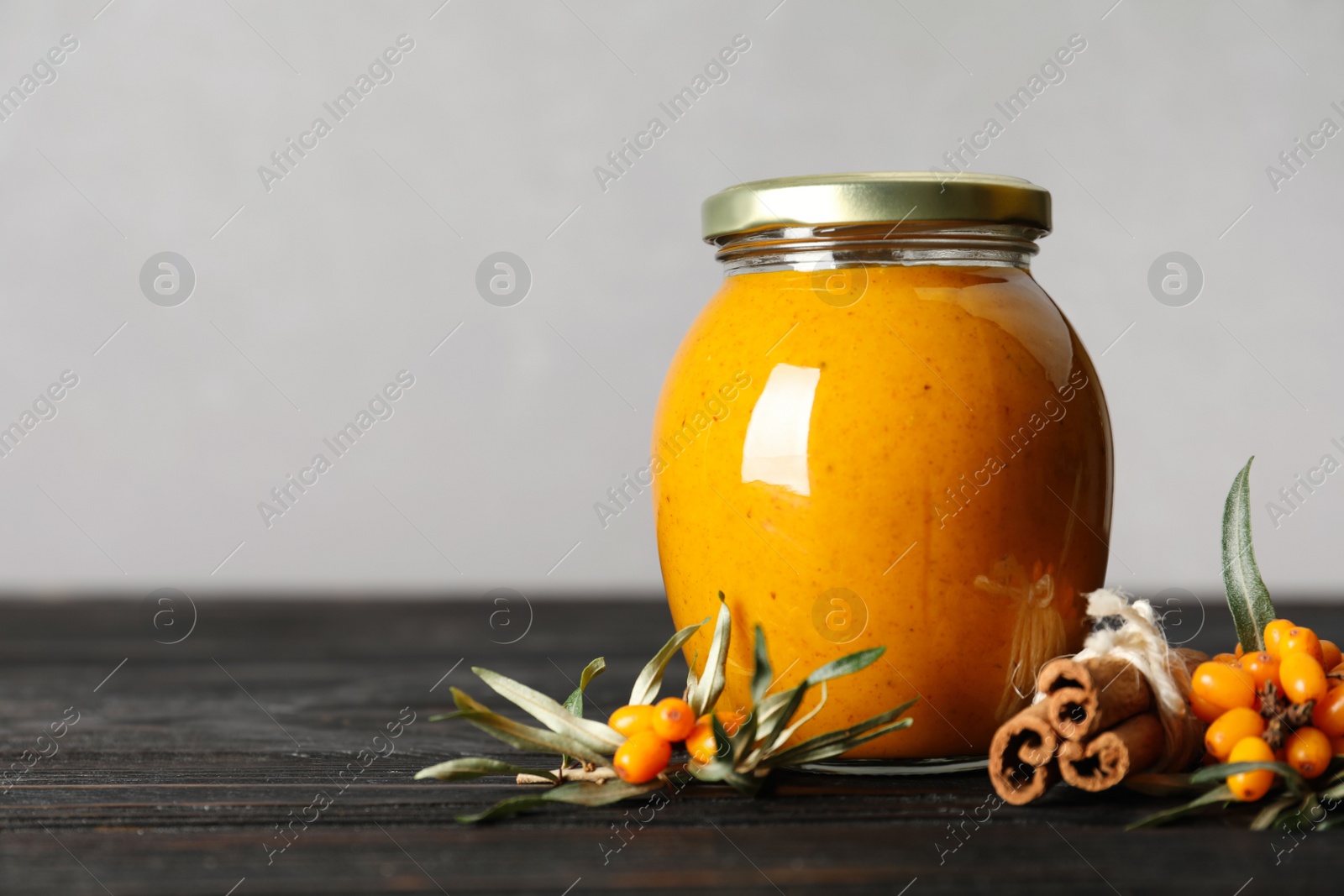 Photo of Delicious sea buckthorn jam and fresh berries on black wooden table. Space for text