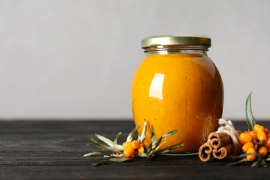 Photo of Delicious sea buckthorn jam and fresh berries on black wooden table. Space for text