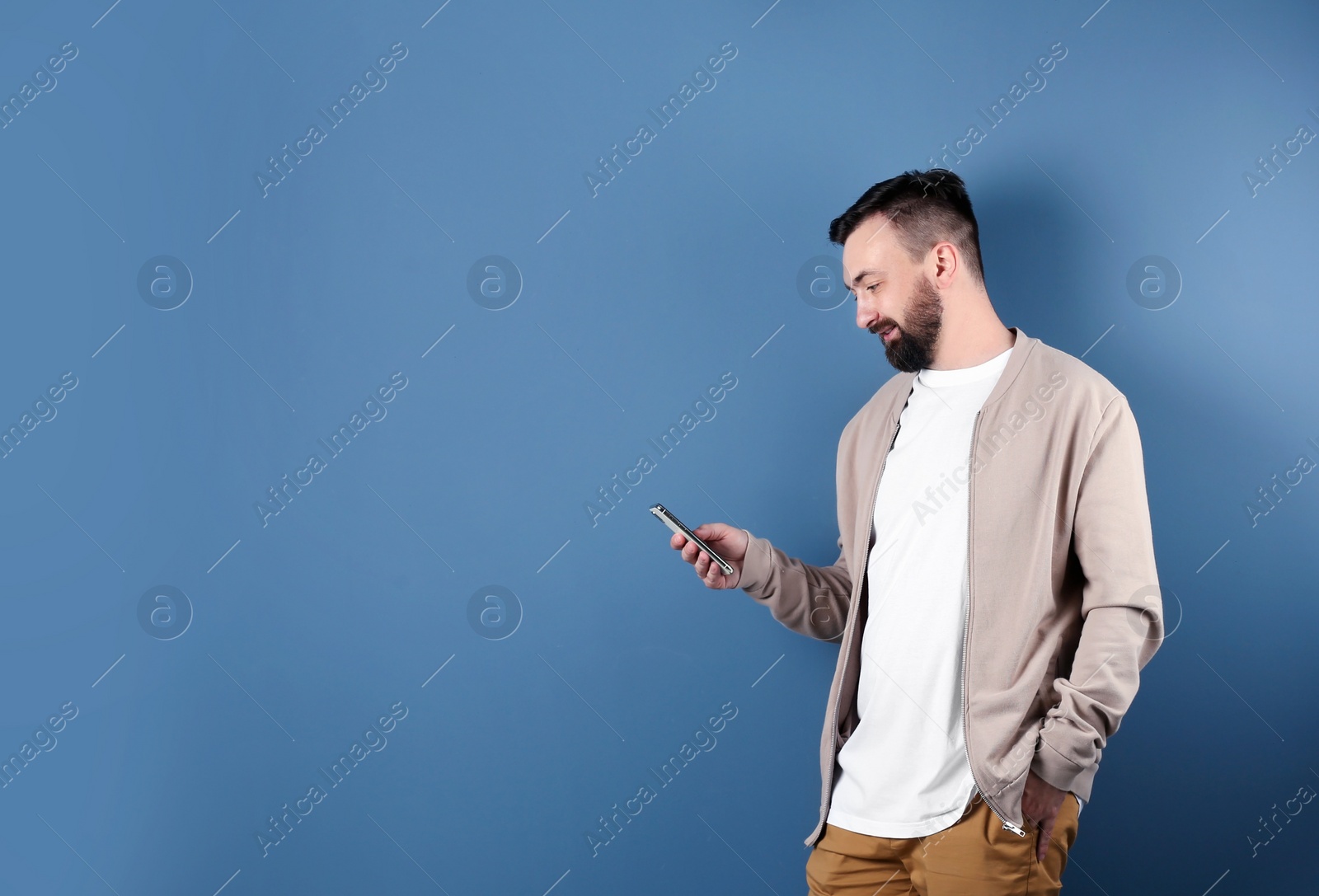 Photo of Portrait of handsome bearded man with mobile phone on color background