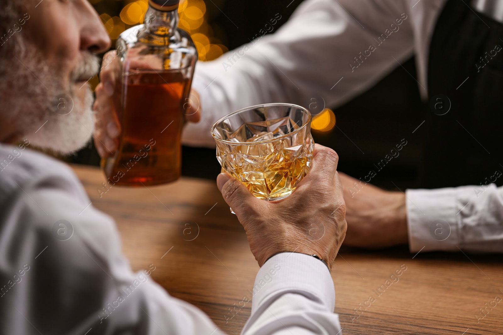 Photo of Bartender pouring whiskey in glass for customer at bar counter, closeup