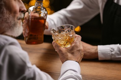 Photo of Bartender pouring whiskey in glass for customer at bar counter, closeup
