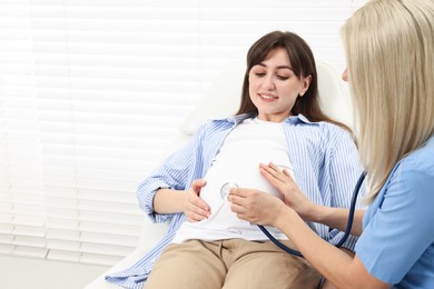 Photo of Pregnancy checkup. Doctor with stethoscope listening baby's heartbeat in patient's tummy in clinic. Space for text