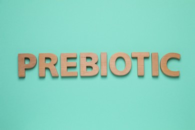 Photo of Word Prebiotic made of wooden letters on turquoise table, flat lay
