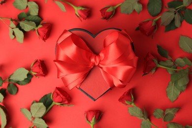 Heart shaped gift box with bow and beautiful roses on red background, flat lay