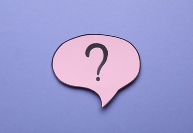 Paper speech bubble with question mark on violet background, above view