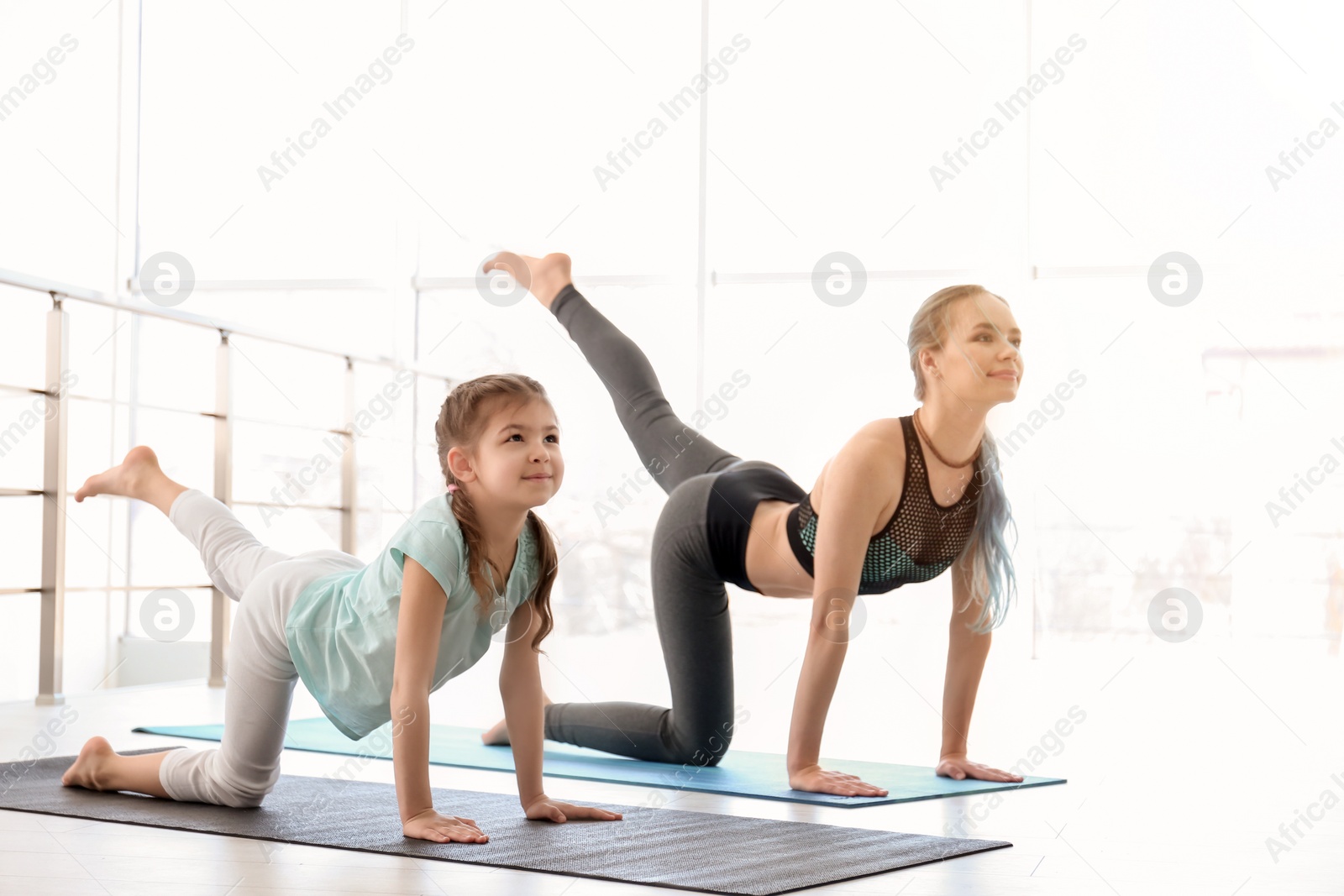 Photo of Little girl and her teacher practicing yoga in gym