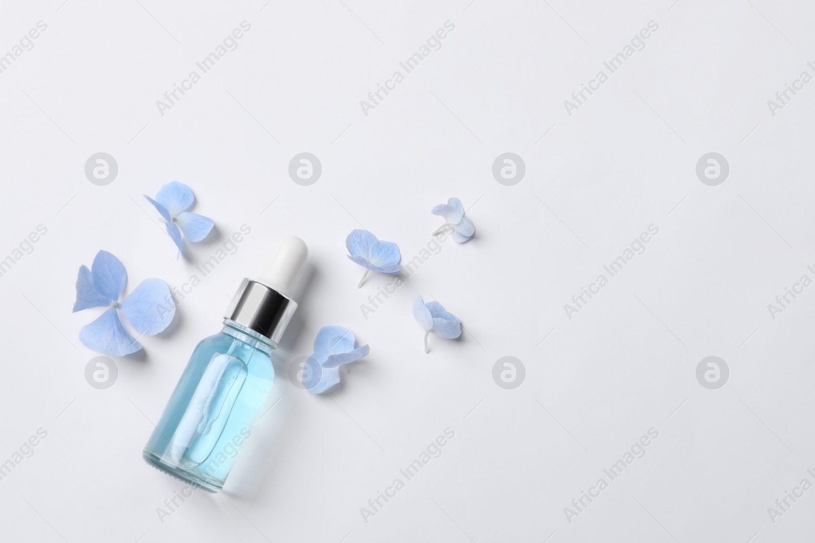 Photo of Bottle of cosmetic serum and beautiful flowers on white background, flat lay. Space for text