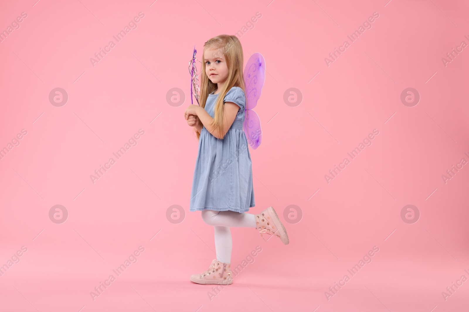 Photo of Cute little girl in fairy costume with violet wings and magic wand on pink background