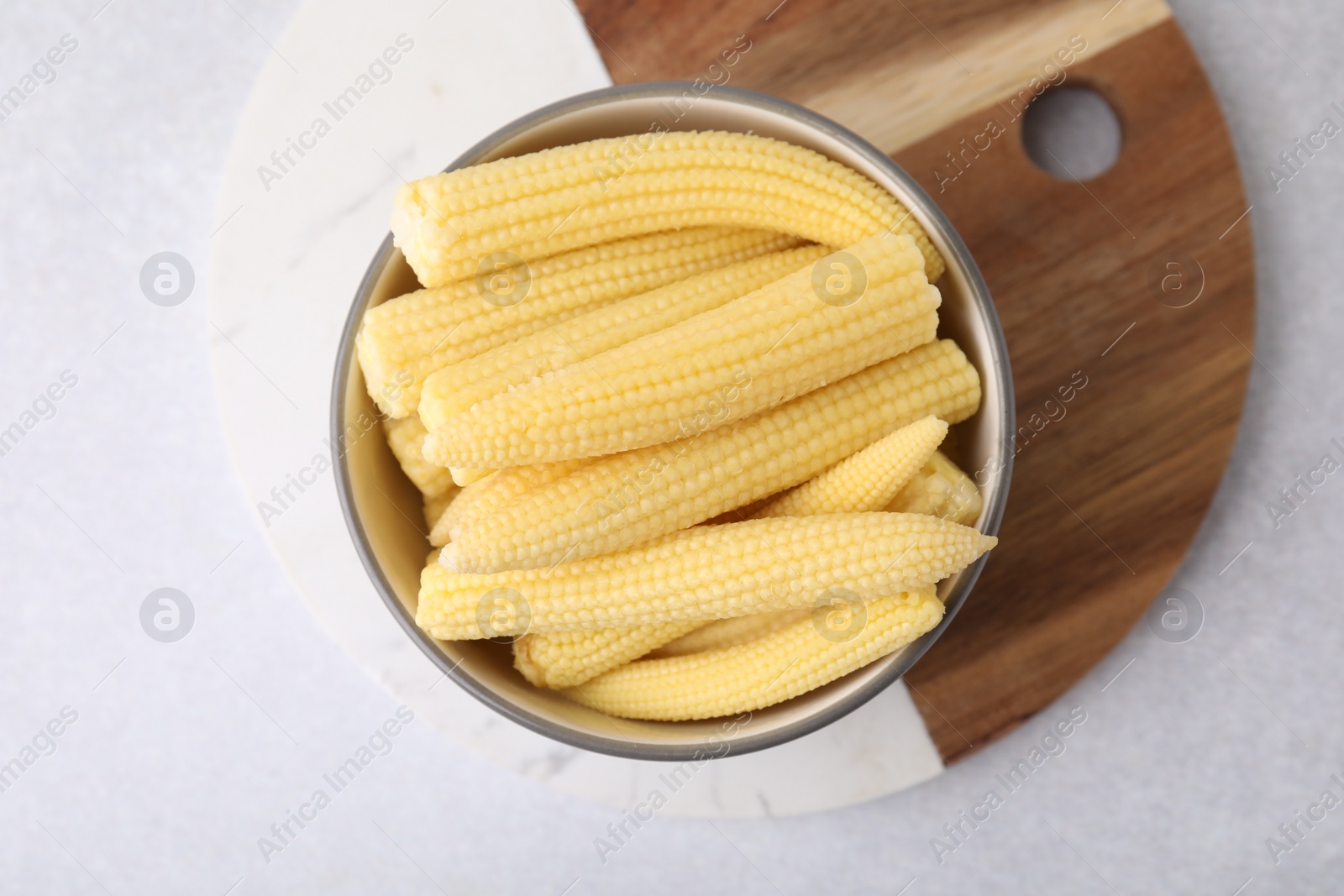 Photo of Tasty fresh yellow baby corns in bowl on white table, top view