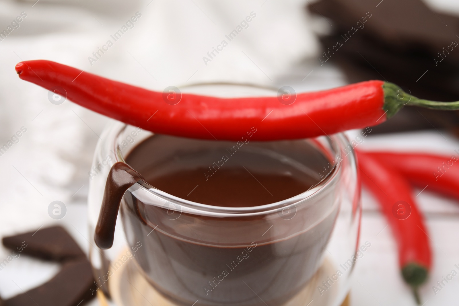 Photo of Glass of hot chocolate with chili pepper on white table, closeup