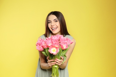 Photo of Portrait of beautiful smiling girl with spring tulips on yellow background. International Women's Day