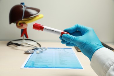 Liver Function Test. Laboratory worker with tube of blood sample, form and model of liver at table, closeup