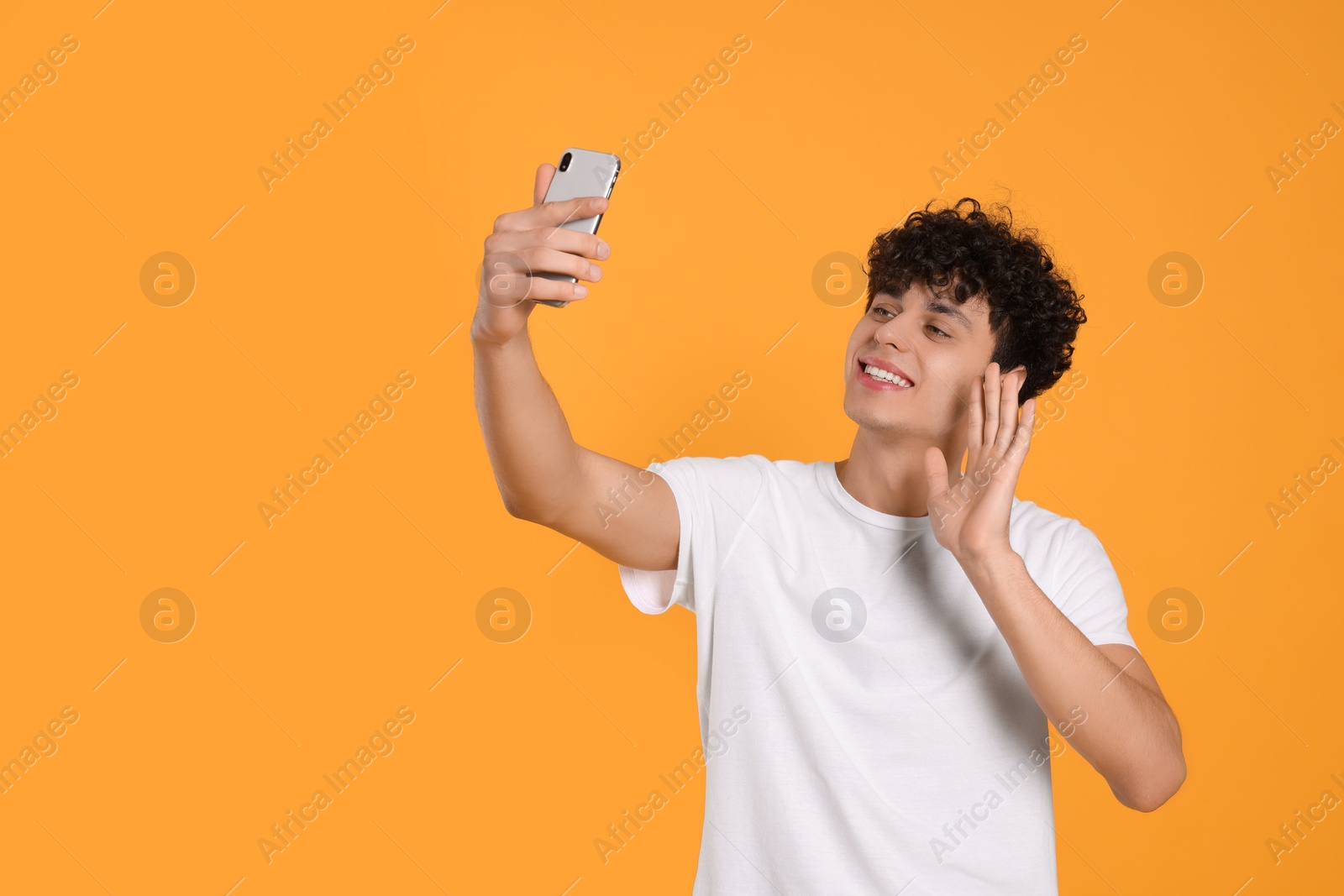 Photo of Handsome young man having video chat on smartphone against orange background. Space for text